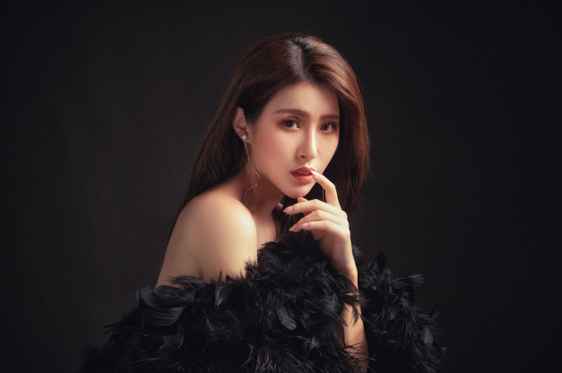 Asian woman with brown hair and black feather boa