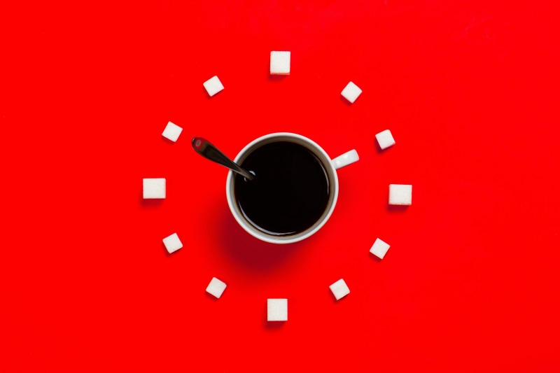 Coffee cup and sugar cubes arranged like a clock on a red background