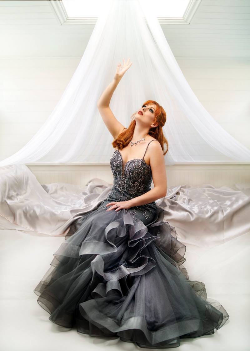 Redhead woman in a sparkly grey gown reaching up