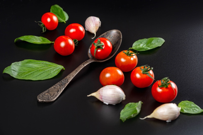 Tomatoes, Garlic, Basil, and Spoon on Black
