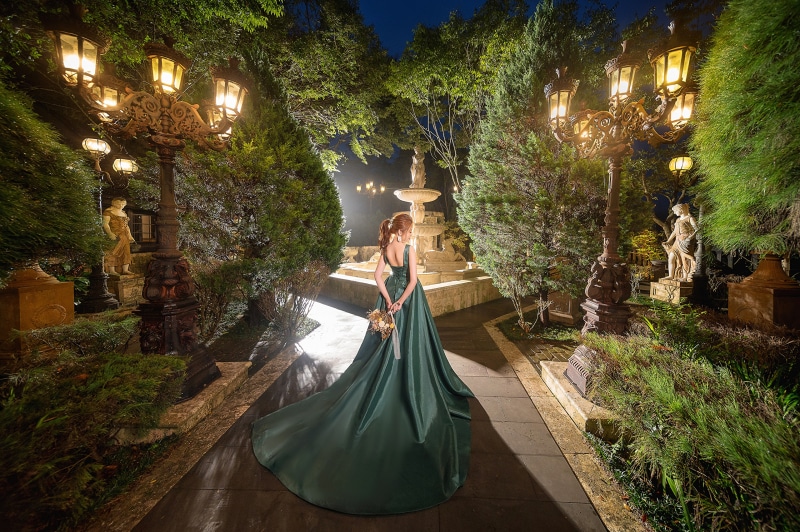 Woman in green dress holding bouquet in garden at night