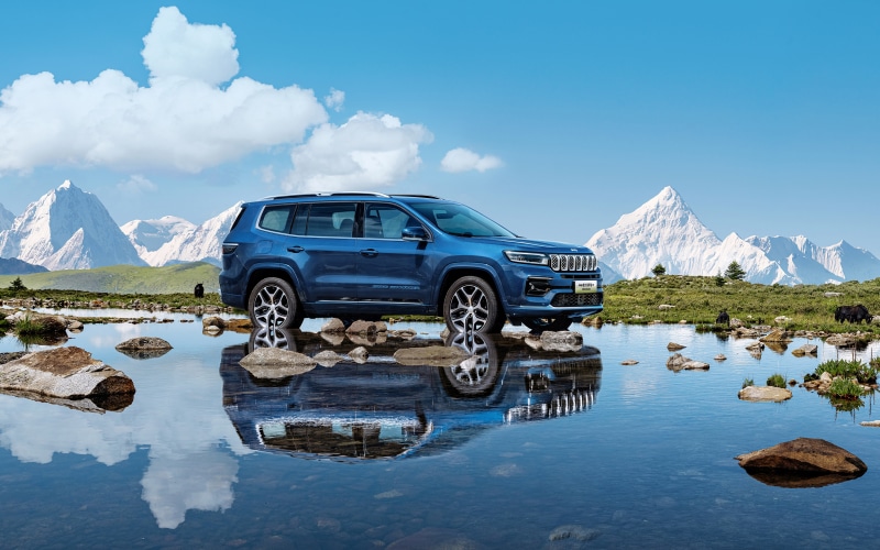 Blue Jeep Grand Commander e in a mountain lake reflection