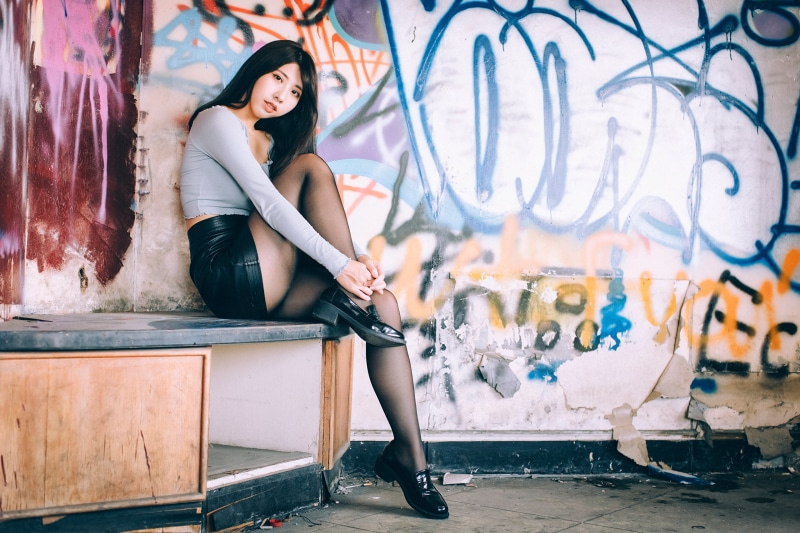 Asian woman in black skirt and stockings posing near graffiti