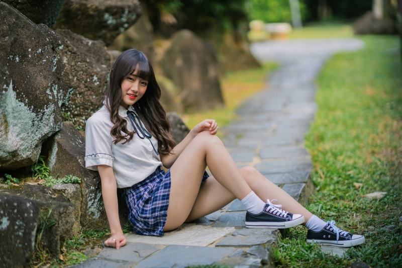 Asian girl in school uniform sitting by rocks
