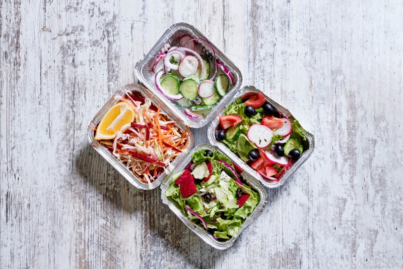 Four foil containers of salads with vegetables