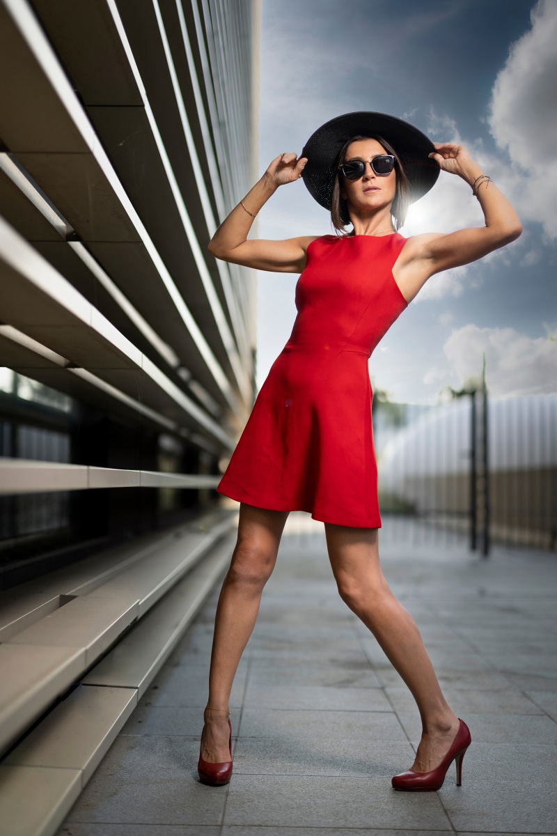 Woman in red dress, hat, and glasses posing outdoors