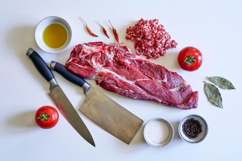 Raw meat, spices, and knives on a white background