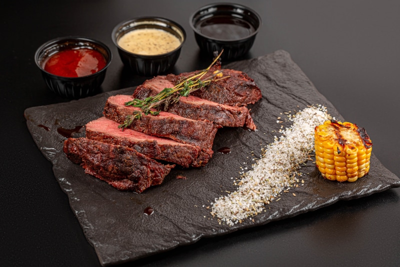 Sliced steak with corn and sauces