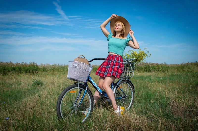 Blonde girl with hat on a bicycle in grasslands