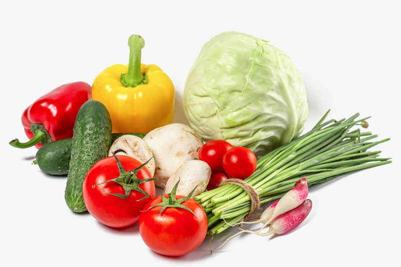 Assortment of fresh vegetables including bell peppers, tomatoes, cabbage, cucumbers, mushrooms, radishes, and scallions on a white background