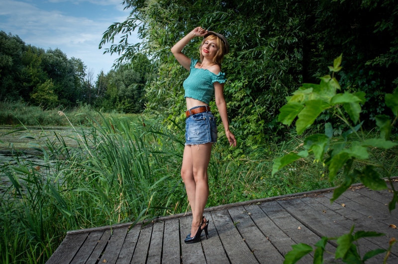 Blonde woman in denim skirt and crop top posing on a boardwalk