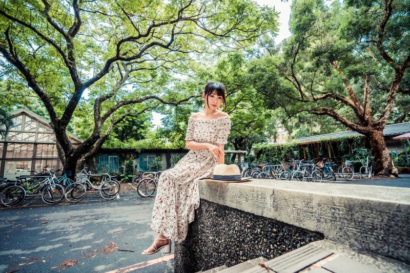 Asian woman in floral dress sitting on wall with hat
