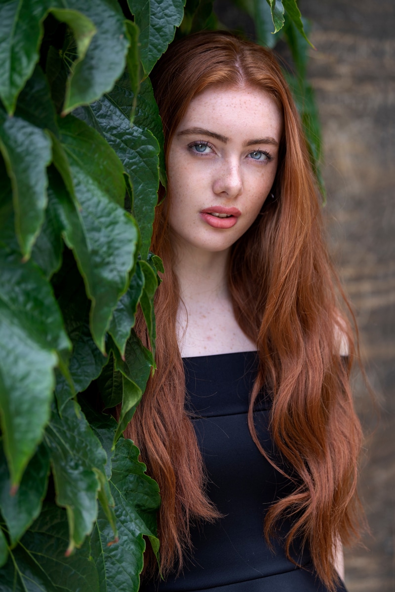 Redhead girl with blue eyes behind foliage