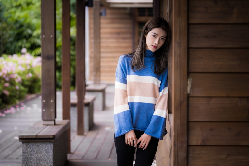 Asian woman in striped sweater leaning against wooden wall