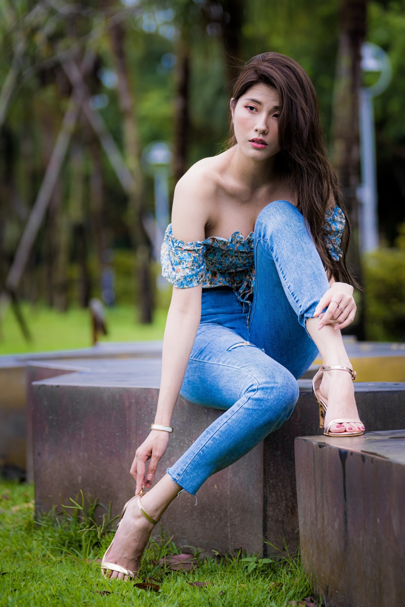 Asian woman in jeans and floral top sitting outdoors