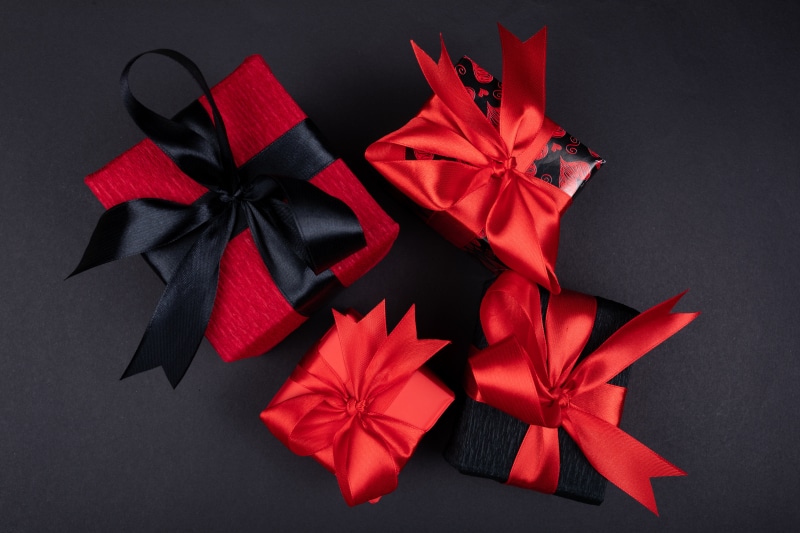 Four gift boxes with red and black ribbons on a gray background