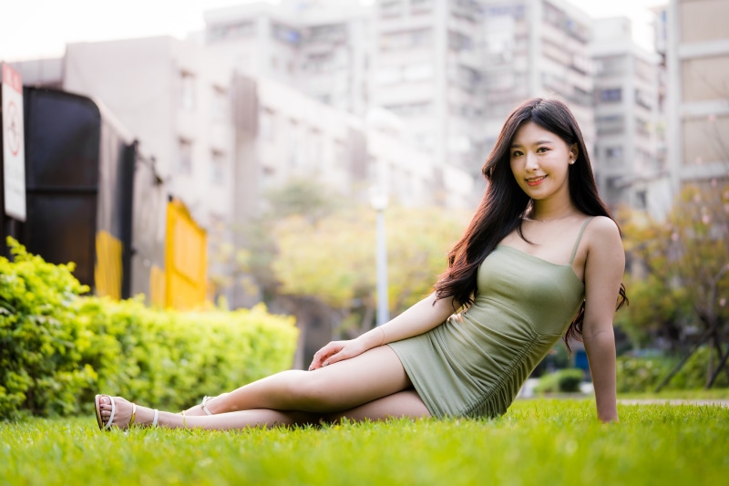 Asian woman in green dress sitting on grass