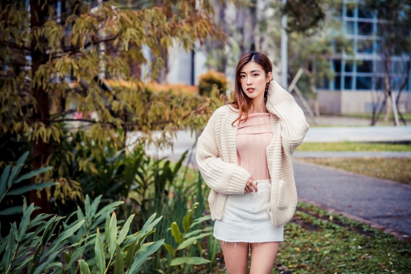 Asian woman in cardigan and skirt posing outdoors