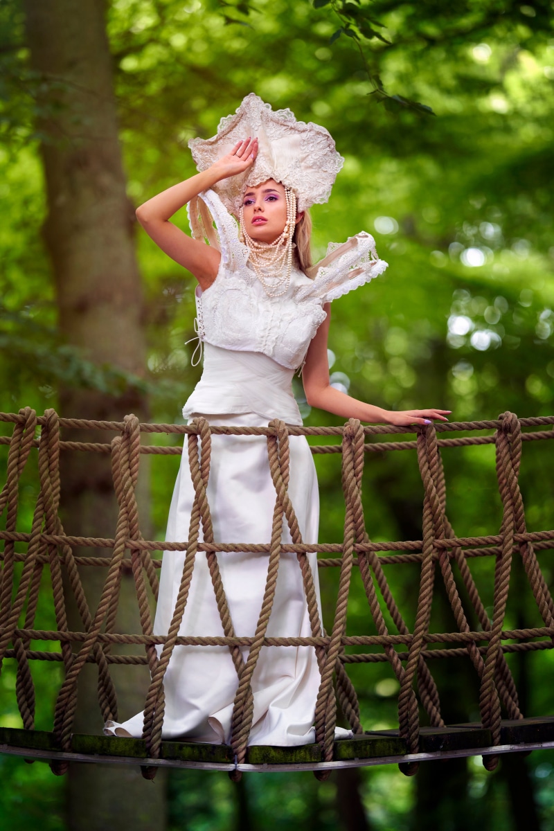Woman in ornate white dress on a rope bridge