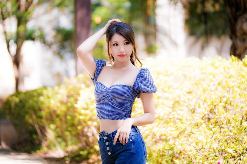 Asian woman in blue gingham top and jeans posing outdoors