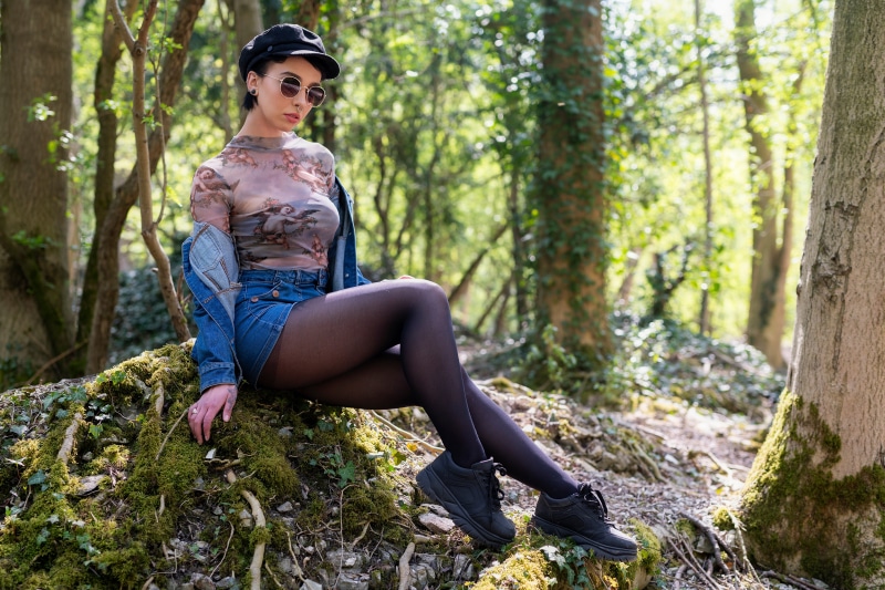 Woman in sheer top and denim skirt sitting in forest