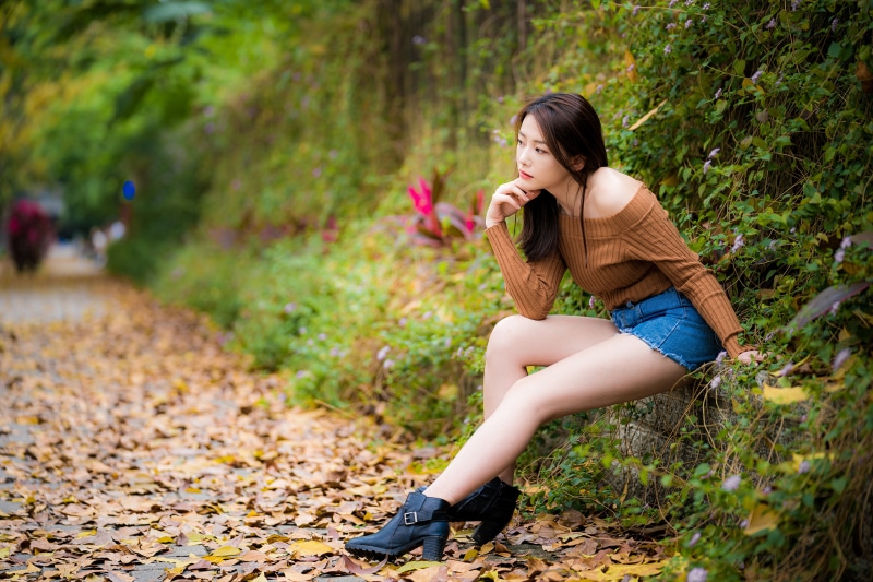 Asian woman sitting on a stone wall with foliage