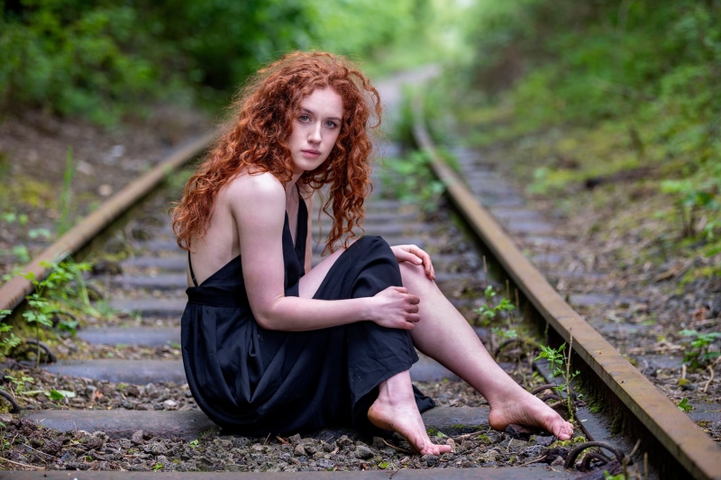 Redhead girl sitting on train tracks