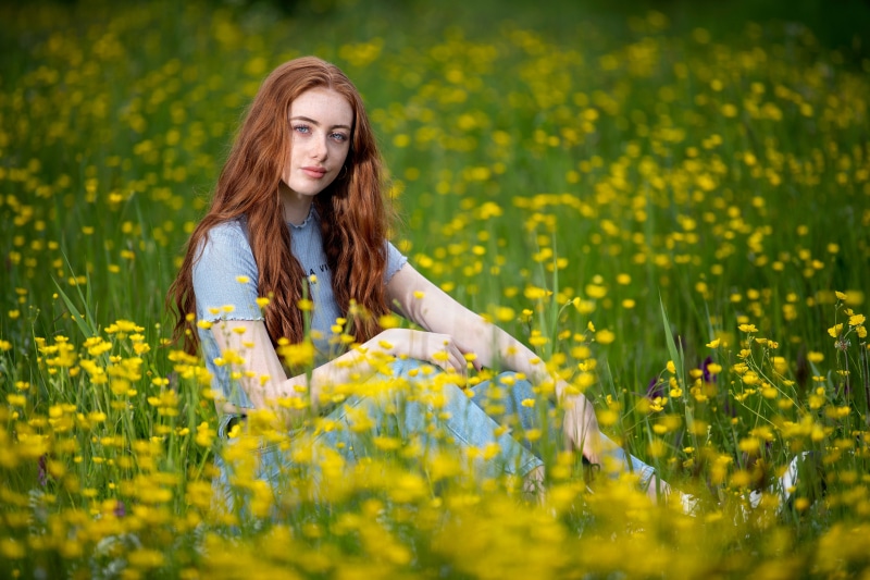 Redhead girl sitting in a field of yellow flowers