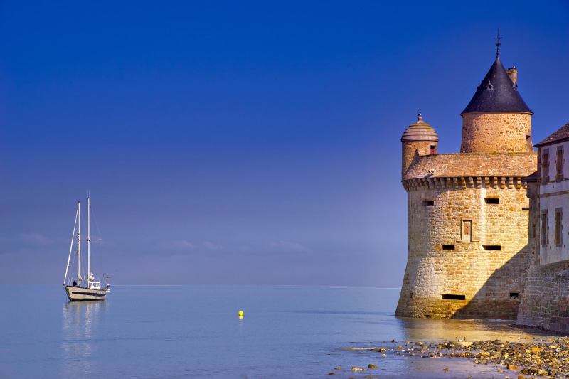 Sailboat near a stone tower by the sea