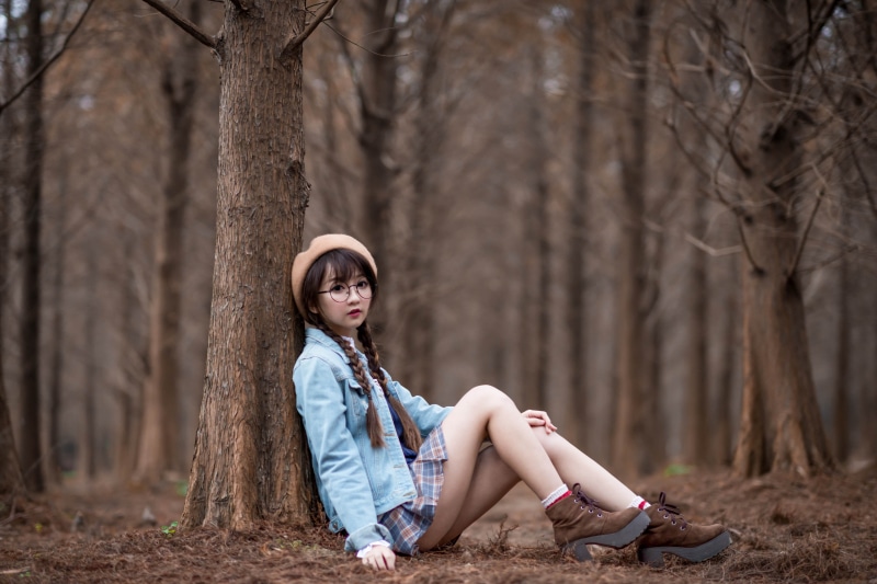 Asian girl with braid hair wearing glasses and beret sitting in forest