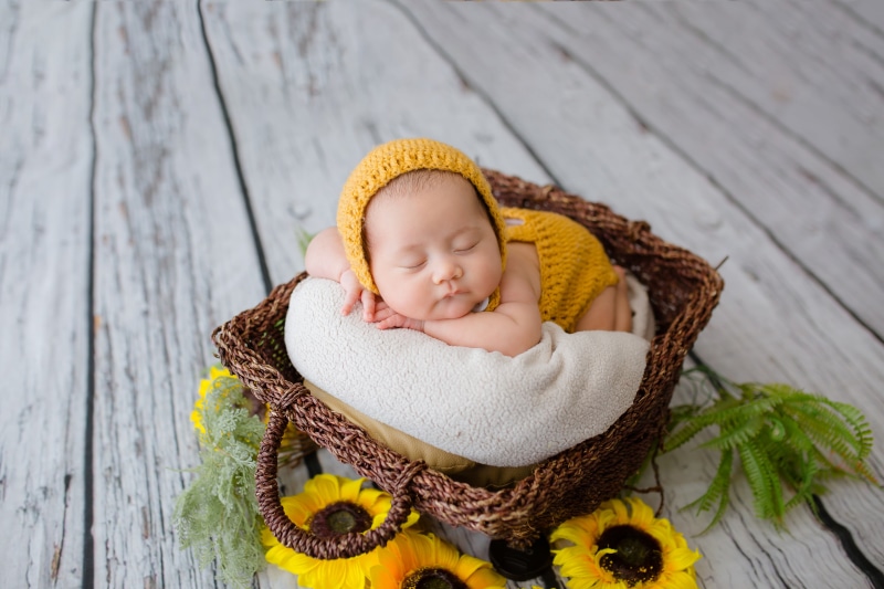 Asian infant sleeping in a wicker basket with sunflowers