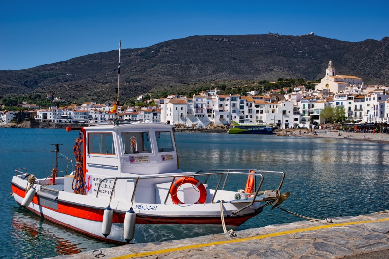 Boat docked in Cadaqués, Spain with coastal town and mountain background