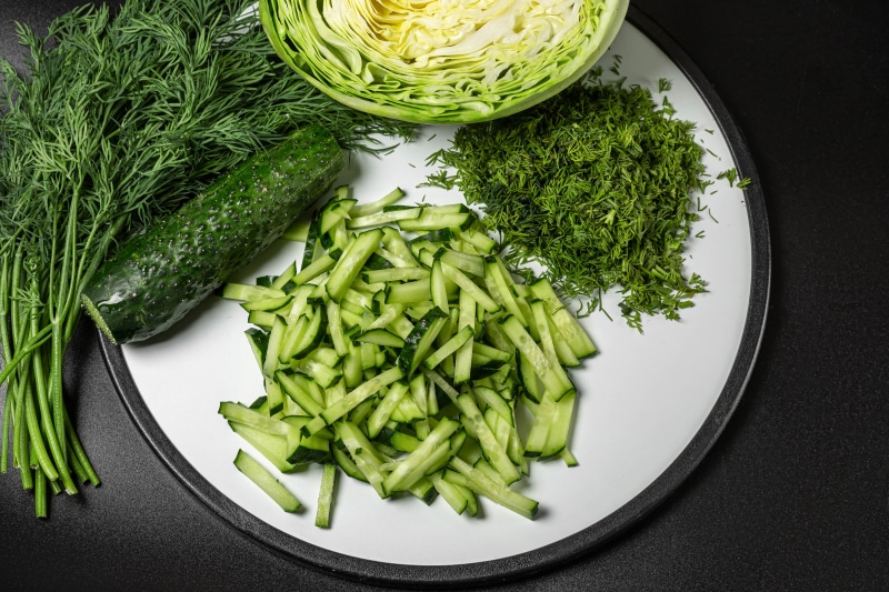 Sliced cucumber, dill, and cabbage on a plate
