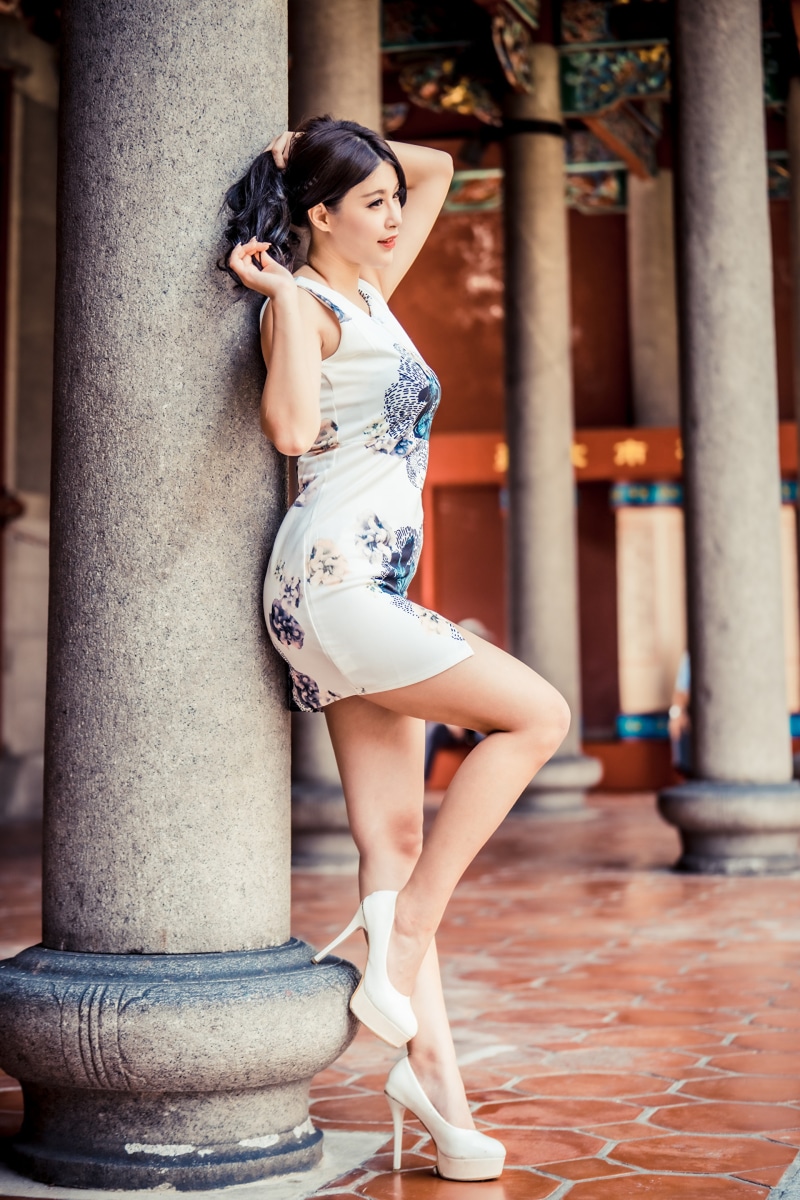 Asian woman in dress and stilettos posing by pillar