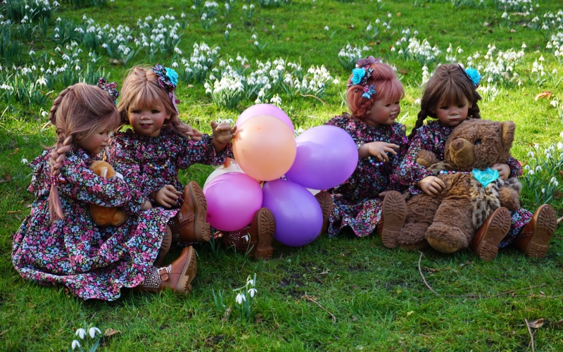 Four dolls with balloons and a teddy bear in a park