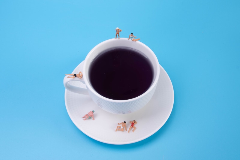 Miniature people sunbathing on a coffee cup and saucer