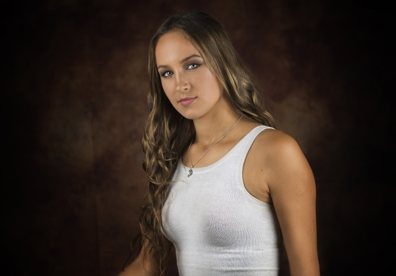 Woman with brown hair wearing a white singlet and necklace