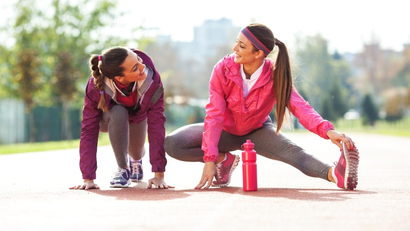 Two women stretching and smiling outdoors
