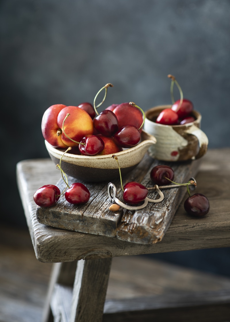Cherries and peaches in bowls on wooden planks