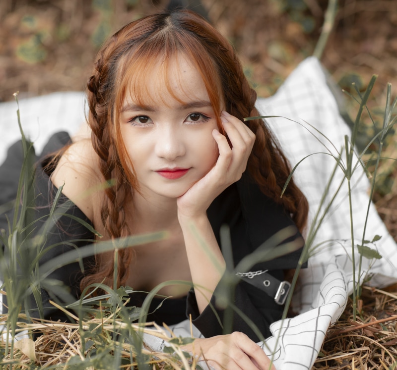 Asian woman with braided brown hair lying in grass