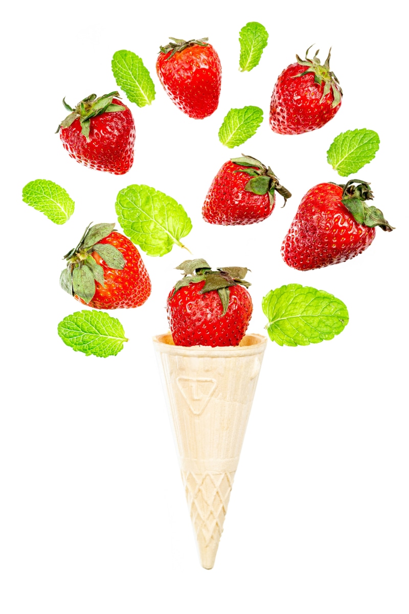 Strawberries and mint leaves falling into an ice cream cone