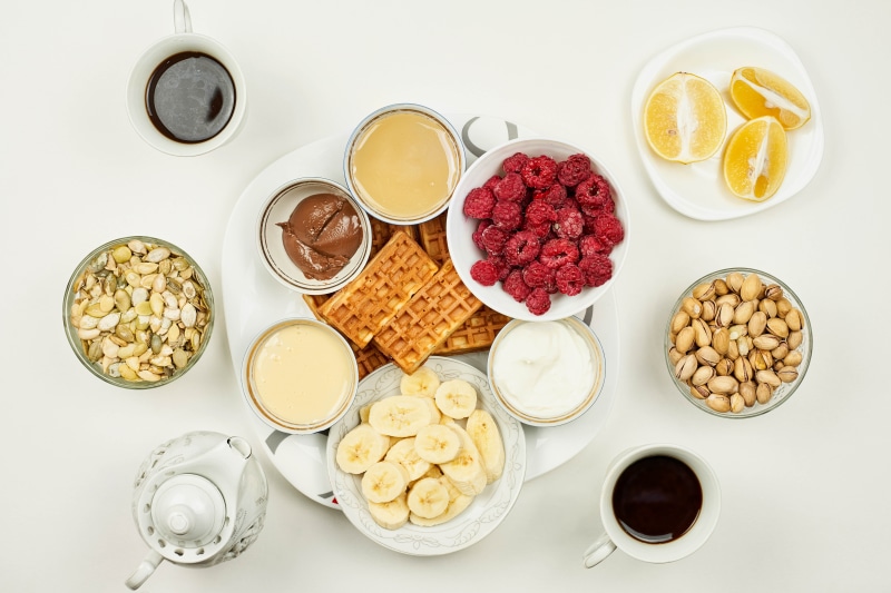 Breakfast spread with waffles, fruits, nuts, and coffee