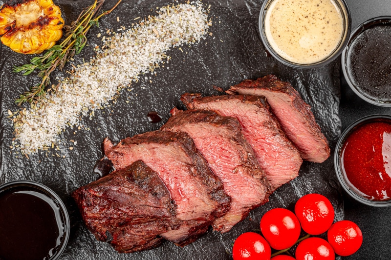 Sliced steak with sauces and grilled corn