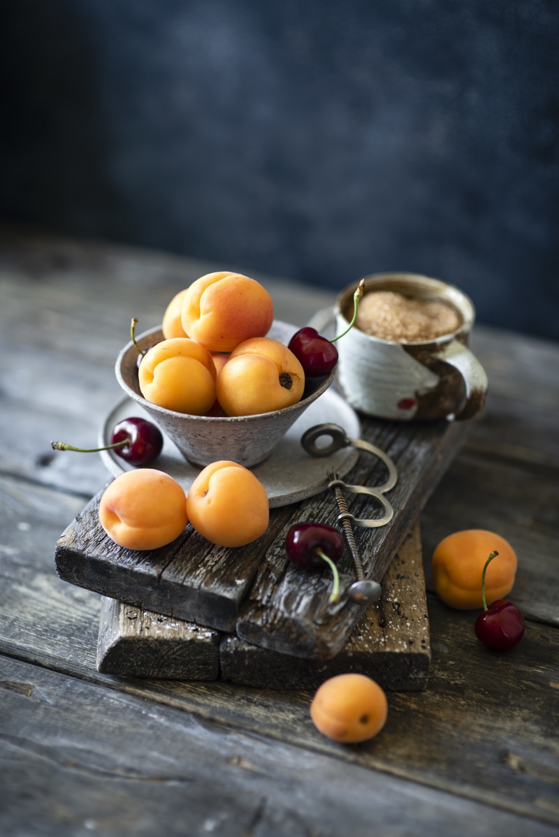 Apricots and cherries with a mug of sugar on wooden planks
