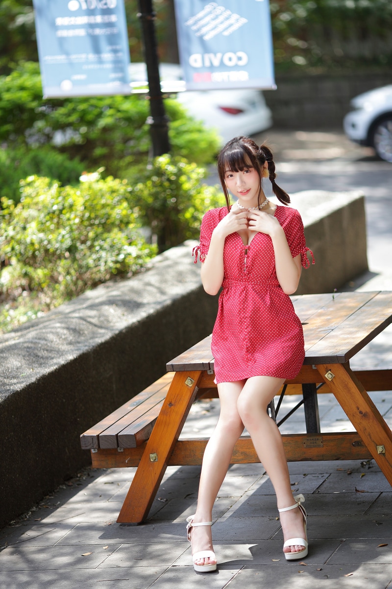 Asian woman in red polka dot dress sitting on a bench