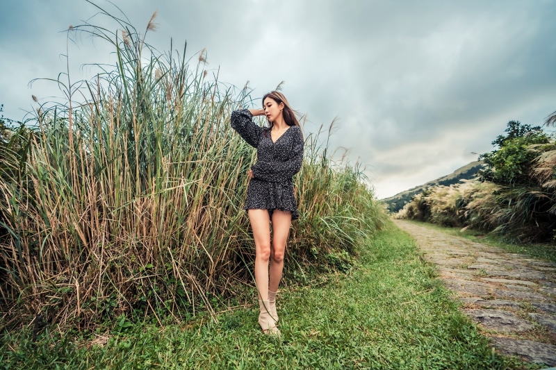 Asian woman in a dress posing near tall grass