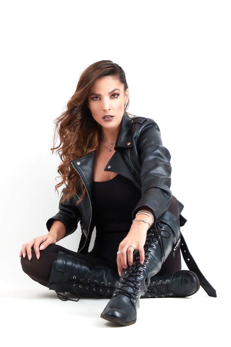 Woman in leather jacket and boots sitting on white background