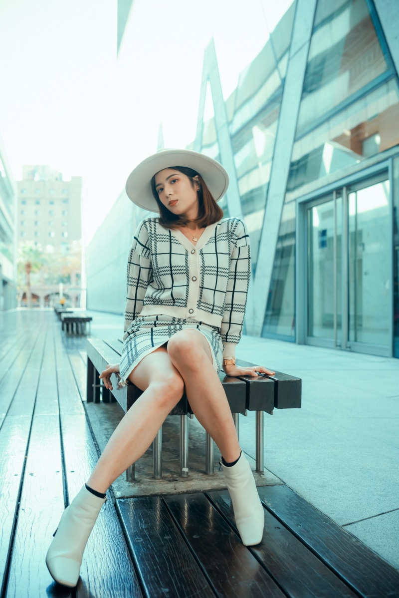 Asian woman wearing a hat and plaid outfit sitting on a bench