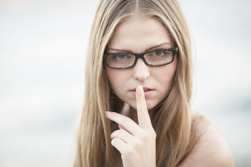 Woman with glasses making a shushing gesture
