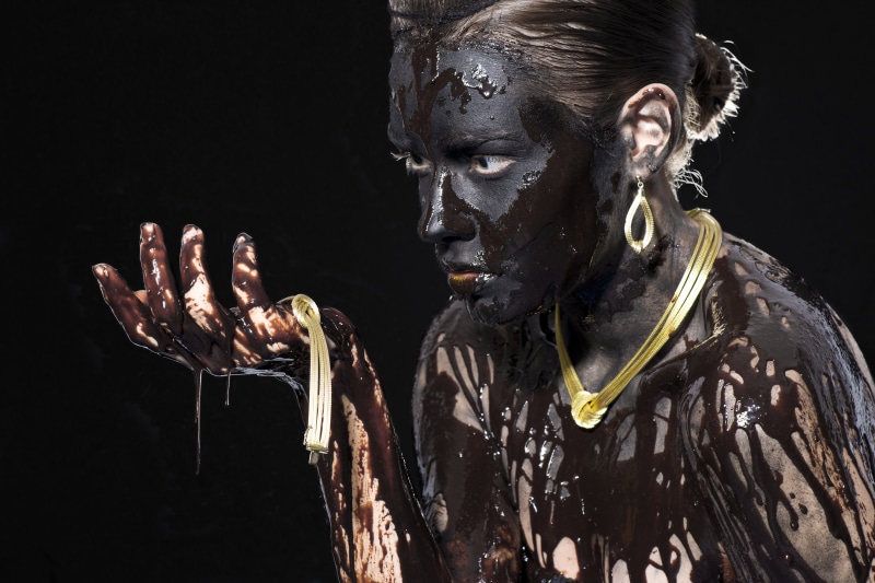 Woman covered in dark mud with gold jewelry